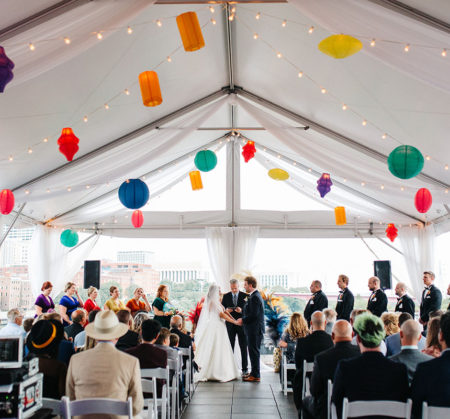 Colorful paper lanterns and stringlights decorate roof of tent for wedding ceremony