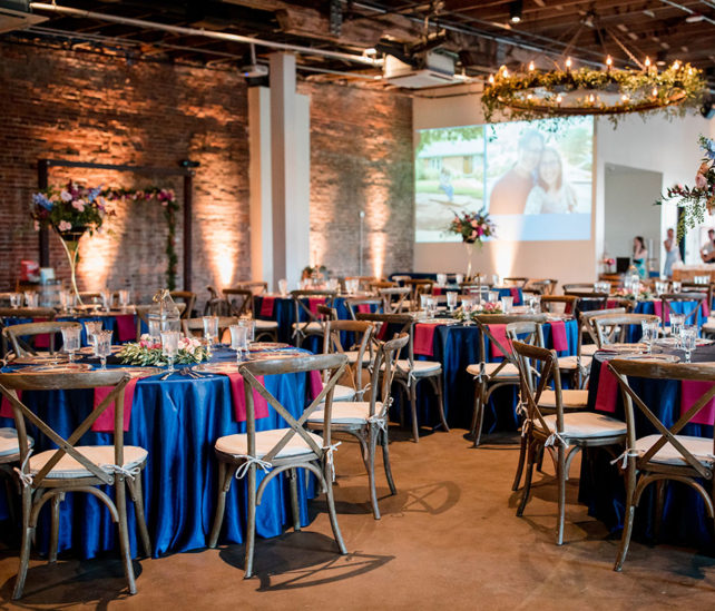 Wedding reception setup with blue table linens and projected slideshow of couple on the wall