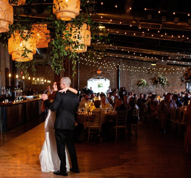 Bride and groom share first dance under bamboo pendant lights decorated with greenery