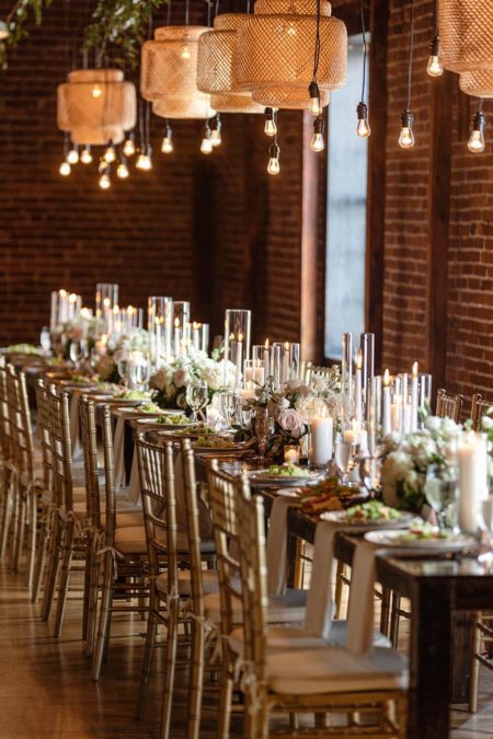 Wedding reception setup at Cannery Ballroom with farmhouse tables, chiavari chairs, bamboo pendants, and string lights