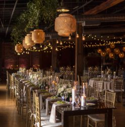 Wedding reception setup at Cannery Ballroom with farmhouse tables, chiavari chairs, bamboo pendants, and string lights