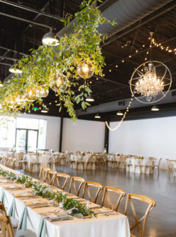 Farmhouse table at wedding reception with glass globe lighting and greenery hanging above