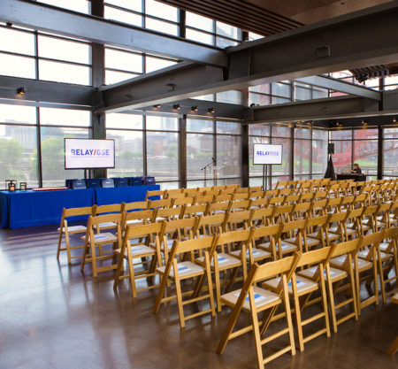 Presentation-style corporate event setup with folding chairs and video screens
