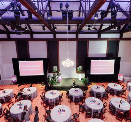 Corporate event dinner setup with stage for speakers, two large screens for video projection, and Maria chandelier