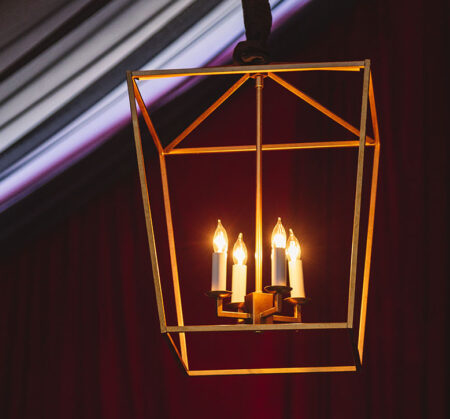 A gold lantern-shaped geometric pendant with open sides and four candle-shaped lights in the center