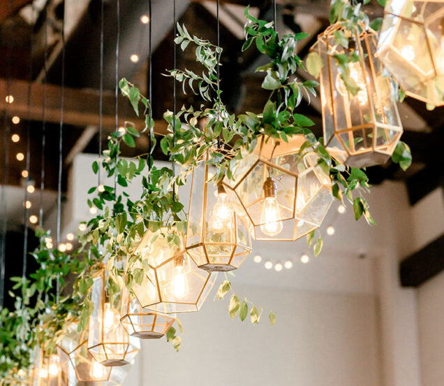 A row of gold geometric shaped terrarium-style pendant lights wrapped in greenery