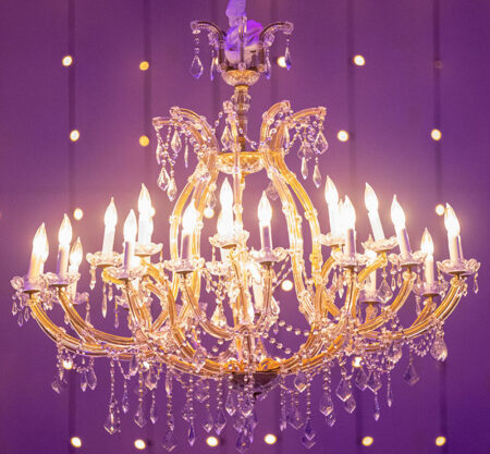 Close-up of glamorous crystal chandelier hanging in a purple-lit room with string lights lining the back wall