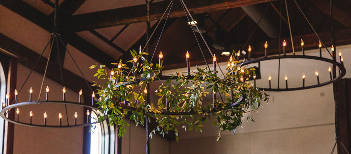 Five large round iron chandeliers with a Renaissance style; some are wrapped in greenery