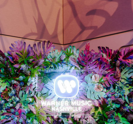 Custom Warner Music neon LED sign hung at the center of large tropical leaves